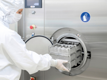 A worker in front of a cleaning and disinfecting machine preparing an order for cleaning. 