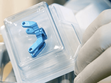 A gloved hand holding a safely packaged implant. The implant is securely packed in a hard blister.