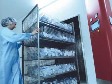 A worker pushing a sterilisation trolley with filled baskets into the EO sterilisation chamber. 