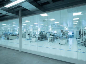 View into the cleanroom area with machinery and production workers in clean room overalls in the background. 