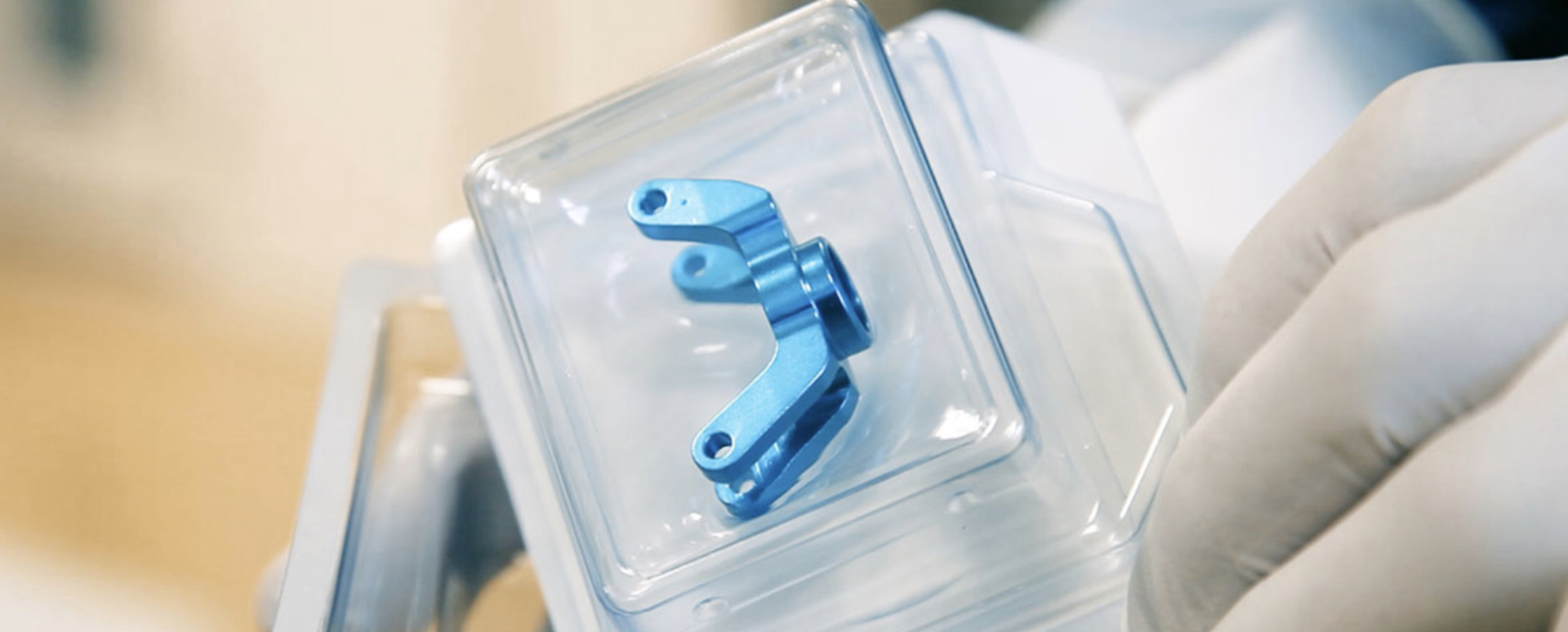 A gloved hand holding a safely packaged implant. The implant is securely packed in a hard blister.